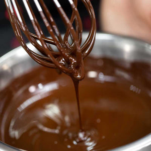 Whisk stirring smooth, melted dark chocolate in a stainless steel bowl during artisan chocolate making process