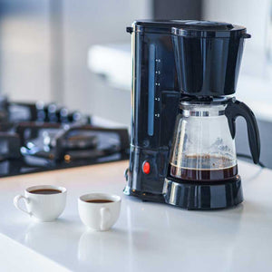 Home drip coffee maker brewing fresh coffee with two cups on kitchen counter — daily at-home coffee routine.