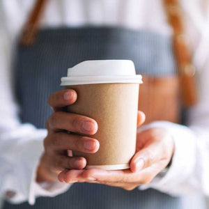 Barista holding takeaway coffee cup in apron — representing daily coffee shop visits and to-go coffee culture.