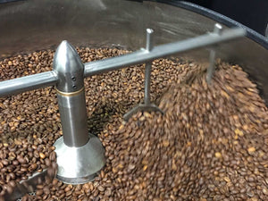 Freshly roasted coffee beans cooling and agitating in a commercial roaster’s cooling tray with spinning metal arms.