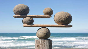 Image of 3 tiers of rocks balancing on wood shelves.  Ocean background.