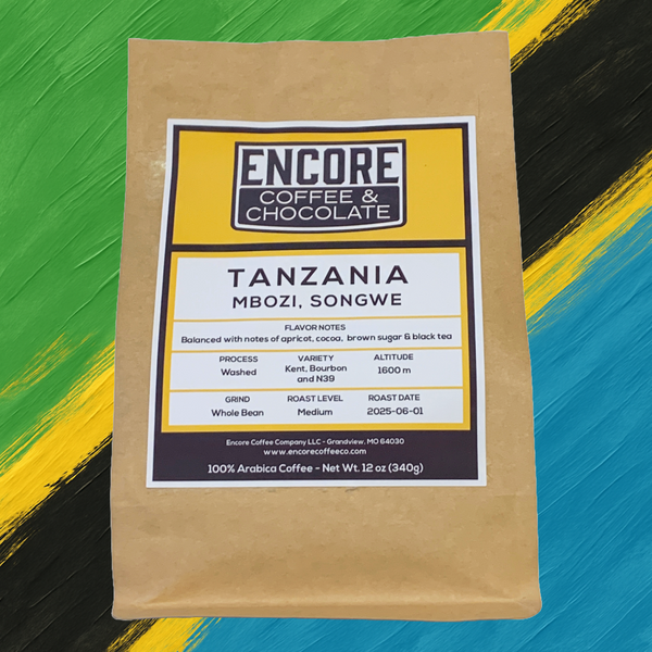 Encore Coffee & Chocolate’s Tanzania coffee bag on a vibrant painted background of green, yellow, black, and blue inspired by the Tanzanian flag. Label details include origin (Mbozi, Songwe), flavor notes (apricot, cocoa, brown sugar, black tea), and roast date 