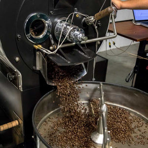 Freshly roasted coffee beans being released from a commercial drum roaster into a cooling tray, highlighting small-batch artisan coffee roasting at Encore Coffee & Chocolate.