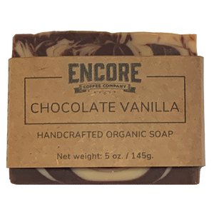 Image of a rectangular bar of Encore's chocolate vanilla soap, wrapped in eco-friendly brown kraft paper with the Encore logo at the top. The soap has a smooth, glossy surface and a creamy beige color. In the foreground, the label reads 'Chocolate Vanilla Soap' in a modern font.