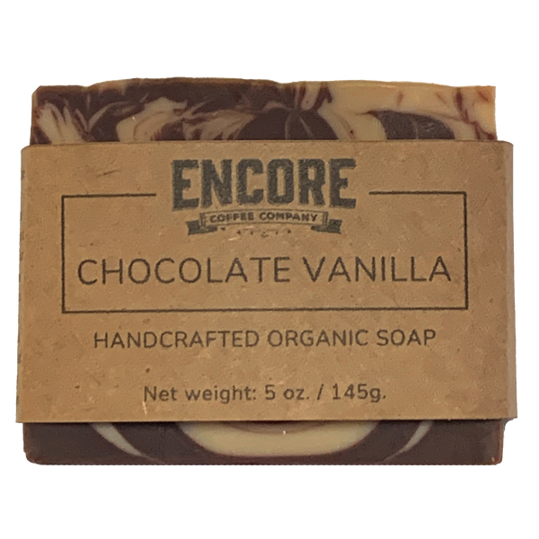 Image of a rectangular bar of Encore's chocolate vanilla soap, wrapped in eco-friendly brown kraft paper with the Encore logo at the top. The soap has a smooth, glossy surface and a creamy beige color. In the foreground, the label reads 'Chocolate Vanilla Soap' in a modern font.